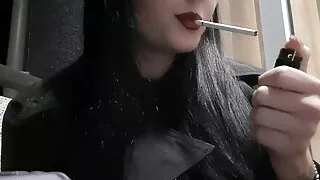 Dominatrix Nika smokes a cigarette on the balcony. Mistress sexy red lips blow smoke in your face
