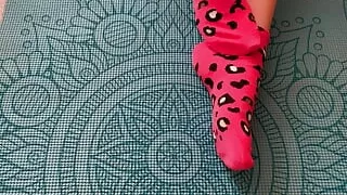 Gloria Gimson in pink socks caresses her feet on a yoga mat