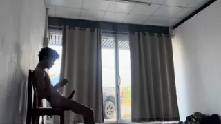 A handsome young man jerks off in front of a glass door.