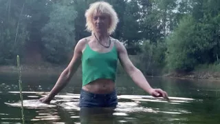 Trans girl swimming in the lake in shorts and green top. Wetlook at th lake.