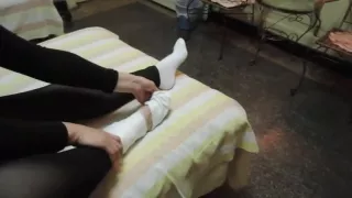 Woman takes off white sock to reveal her bandaged ankle