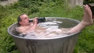 Naked old man rolls around in outside bath tub.