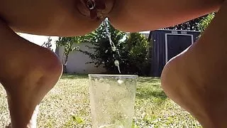 MILF tans naked outside and pissing in a tall glass